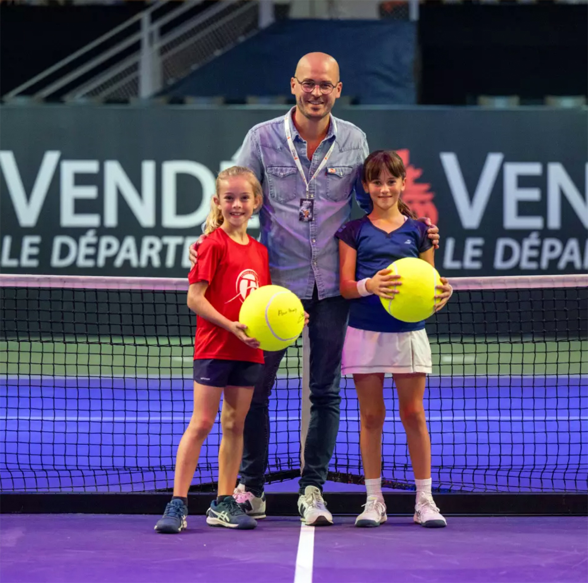 Deux jeunes joueuses de tennis et un adulte posant pour une photographie sur un terrain de tennis